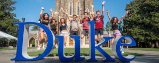 Duke students jumping behind Duke sign